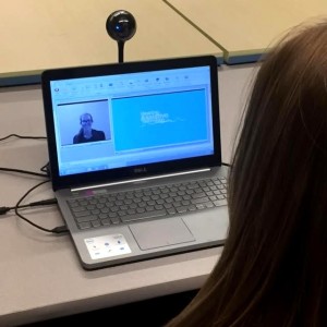 A telerehabilitation session with a video feed and a slide deck is displayed on a laptop.