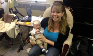 A mother holds an infant in her arm. EEG electrodes are attached and connected to a measuring device.